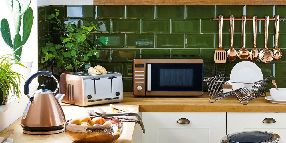 A kitchen counter with a kettle, a toaster, a microwave and hanging utensils